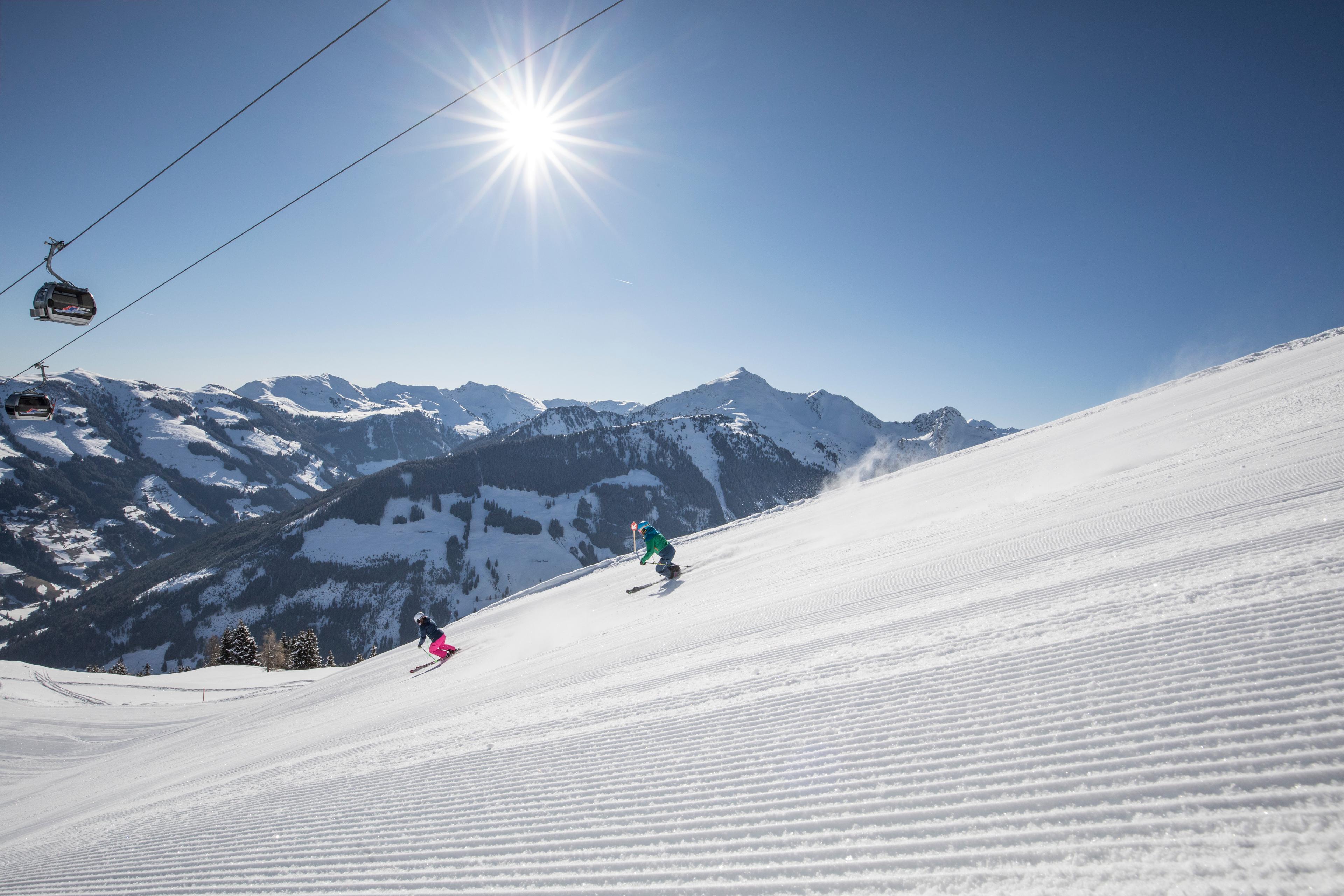 2 skiiers skiing down piste underneath gondola on bluebird day in Austria