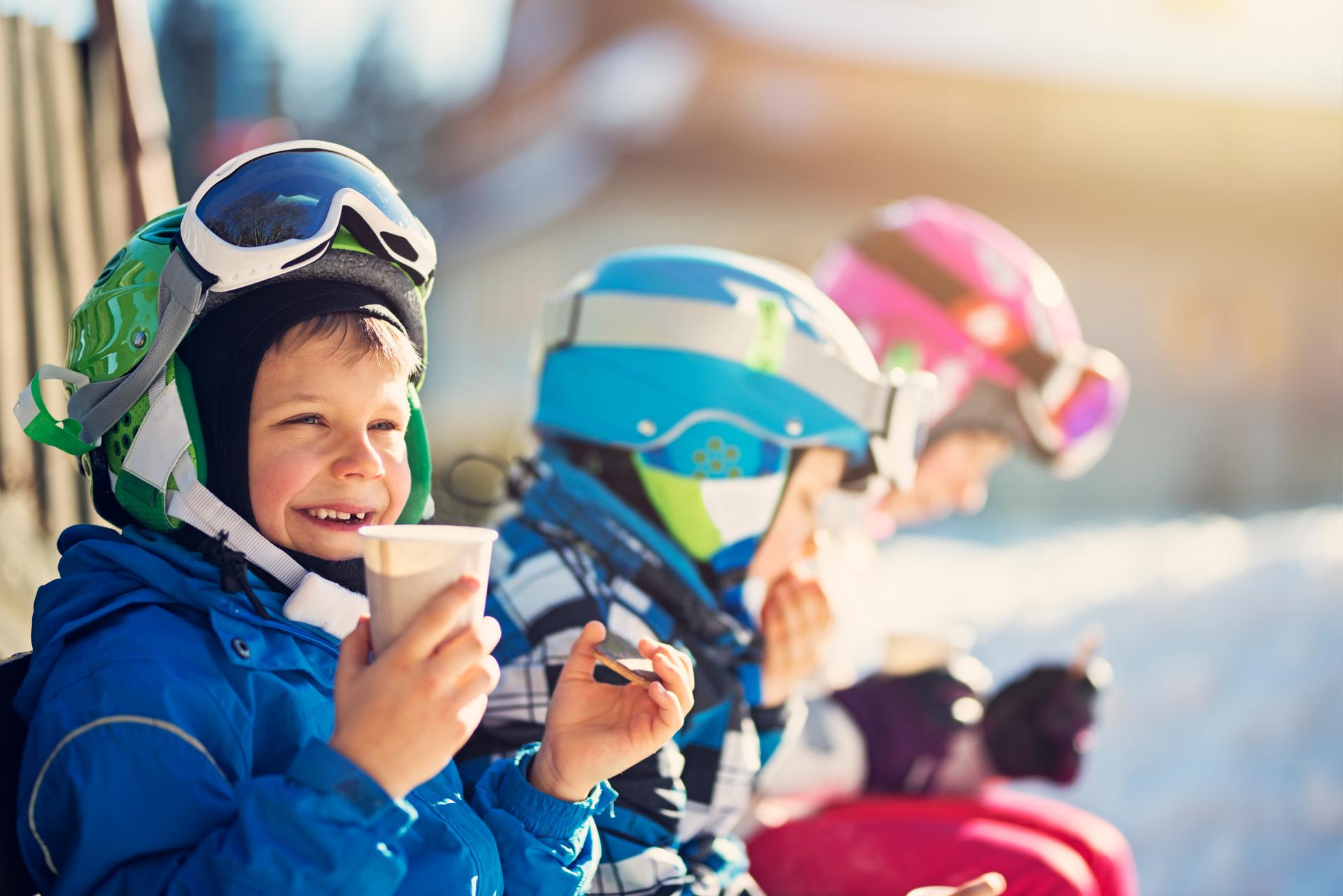 Three kids are enjoying a hot drink and a biscuit on their ski holiday